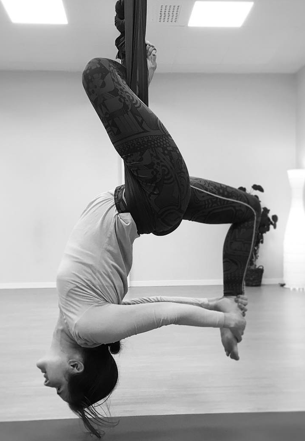 Author A. K. Hudson practicing aerial yoga, suspended upside down.