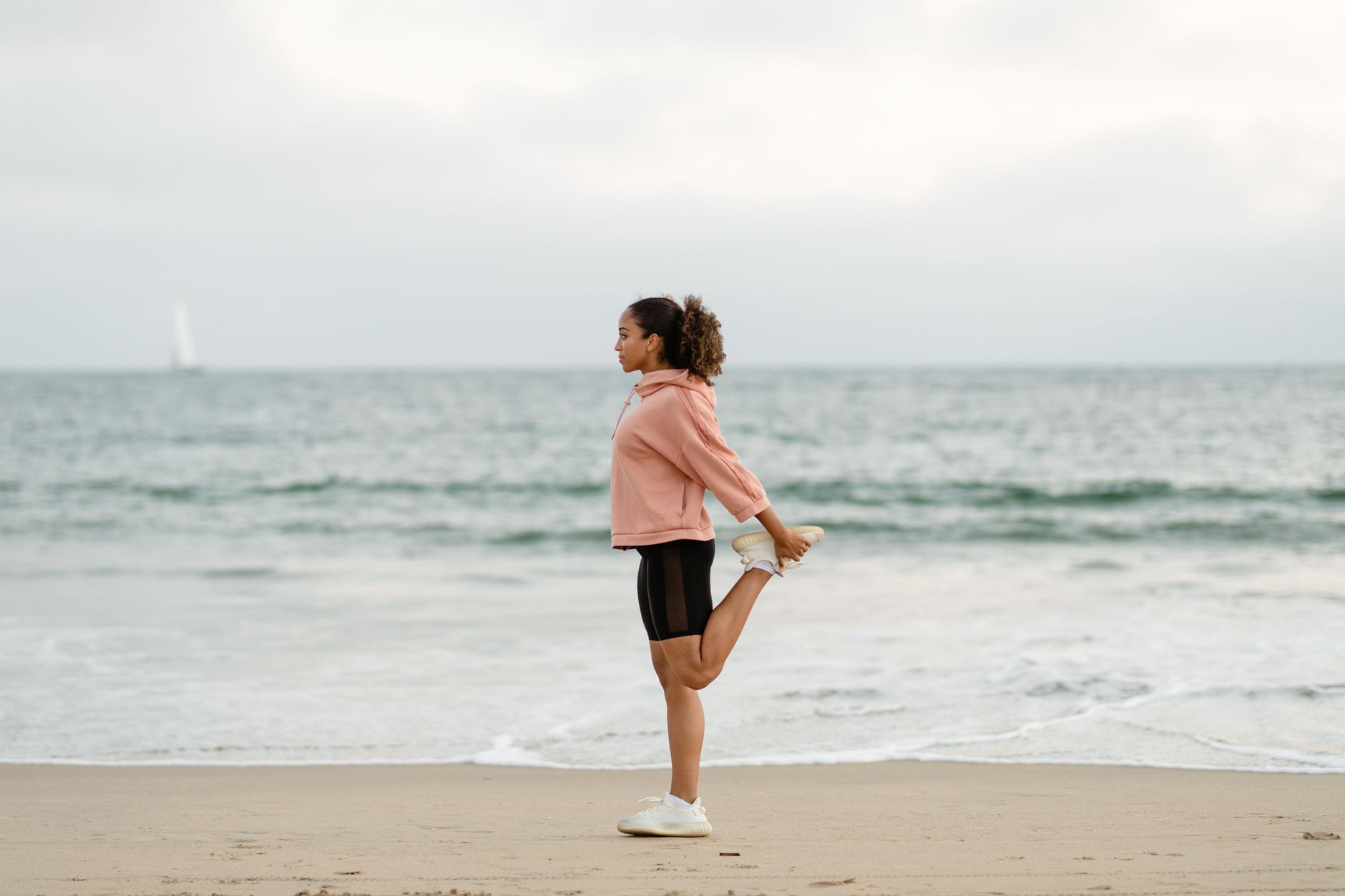 Image of a woman on a beach standing, stretching her quad.